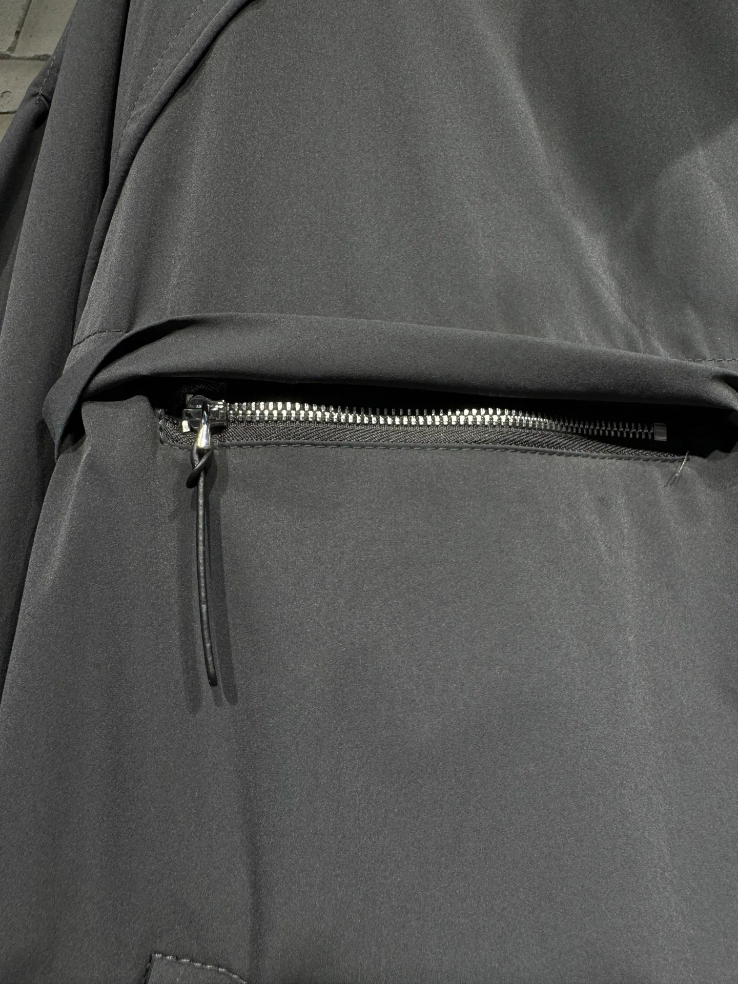 Acne Studios 26SS Large Lapel Short Jacket The fabric is made of 100% nylon (nylon/polyamide fiber) 75D high-density wrinkled nylon. The fabric has been permanently pressed and shaped by high temperature, and washed with high-pressure wrinkles at the factory to form its own irregular texture, permanently retaining the wrinkled texture, which will not disappear after washing. Matte matte coating removes the plastic glossy surface of nylon itself to create a low-key matte paper feel. Three-proof micro-coating, weak waterproof, anti-fouling, anti-static treatment, not easy to get dust. The interior is made of full-width mesh Breathable nylon lining, which reduces the stickiness of the nylon fabric to the body, improves air circulation, prevents sweating from sticking to the skin, and the zipper does not rub against the skin. The version adopts the raglan split topstitching process, and the front and rear panels are divided diagonally to expose even stitching. The three-dimensional dropped shoulders are loose and the fit is increased to increase the margin of movement. The back neckline is three-dimensional and high-density computer embroidered, and the embroidery lines are dense and not prickly. Customized all-metal matte nylon zipper, Genuine Leather embossed brand letters on the zipper leather tab, zipper tape with same color nylon fit to the body, double-locked reinforcement on both sides of the zipper to prevent pulling and tearing. Color: Gray Size: S M L